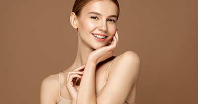 Skin care model. Beautiful young woman with perfect skin touching her face and posing against beige background. Beauty treatment and spa concept.